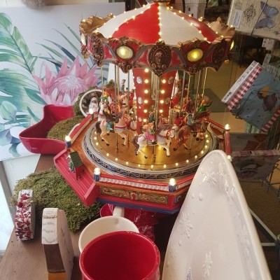 Carrossel decorativo vermelho e dourado com cavalos coloridos e luzes acesas numa mesa com canecas e bandeja branca