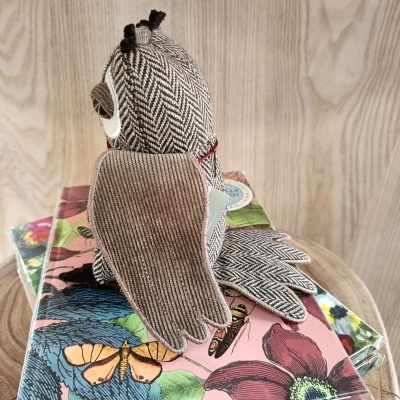 Pelúcia de coruja em tecido com padrão espinha de peixe e veludo cotelê, sobre cadernos florais e borboletas, em madeira clara