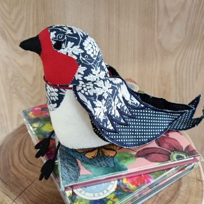 Pássaro decorativo em tecido azul, branco e vermelho sobre caixas florais em madeira clara