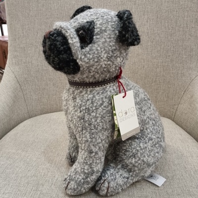 Boneco de cachorro cinzento e preto com coleira castanha e etiqueta sentado numa cadeira cinzenta