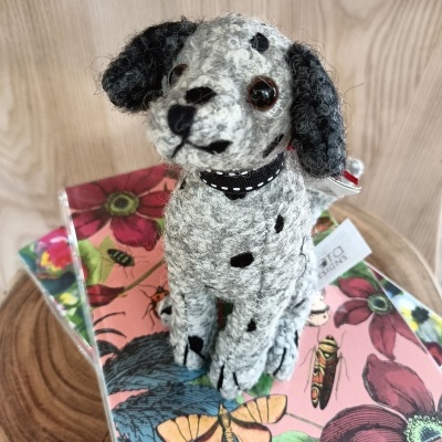 Pelúcia de cão cinzento com manchas pretas sentada sobre capas coloridas com flores e borboletas