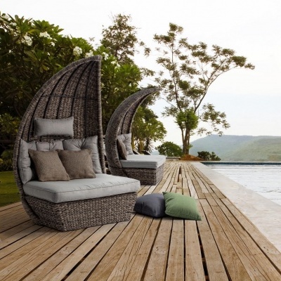 Cadeirões de rattan cinzentos com almofadas ao lado de piscina em deck de madeira