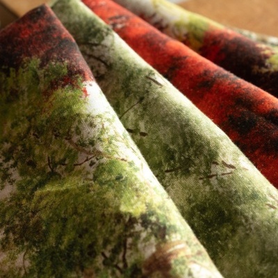 Tecido estampado com desenhos de árvores em várias cores, dobrados sobre superfície de madeira.