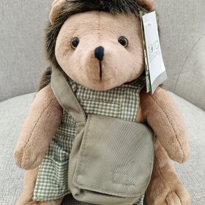 Ursinho de peluche vestido com vestido verde e acessórios cinzentos sentado num sofá cinzento