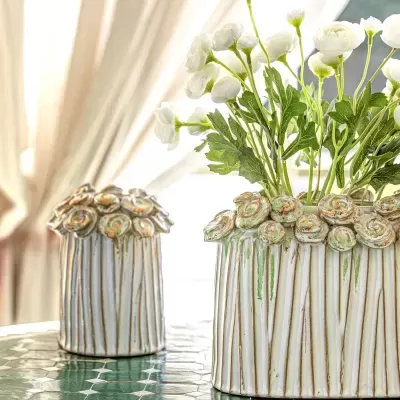 Dois vasos cerâmicos decorativos com rosas em relevo, um com flores artificiais brancas, sobre mesa com azulejos verdes e bege.
