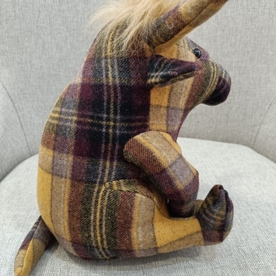 Pelúcia de unicórnio xadrez castanho e amarelo sentada em sofá cinza