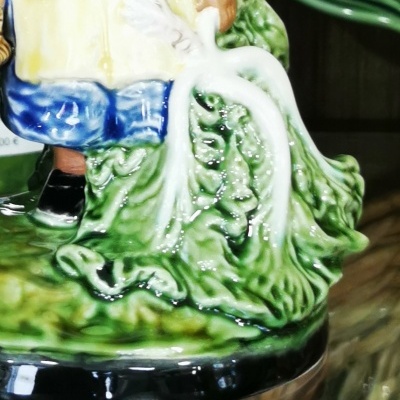 Base cerâmica decorativa com relevo de folhas verdes e parte de figura humana vestida