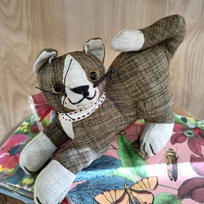 Boneco tecido cão castanho beige olhos plásticos apoiado em caixas metal decoradas flores e borboleta