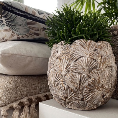 Vaso decorativo com padrão de folhas e planta artificial junto a almofadas em cores neutras