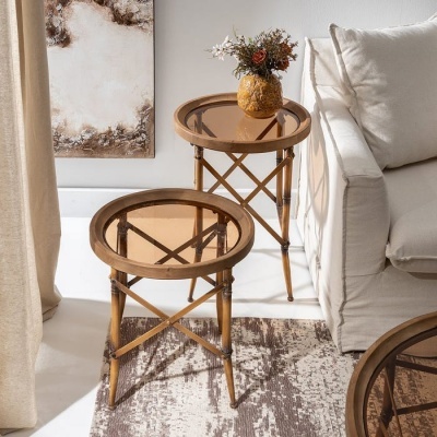 Duas mesas de apoio redondas de madeira clara com tampo de vidro castanho, vaso decorativo e sofá bege