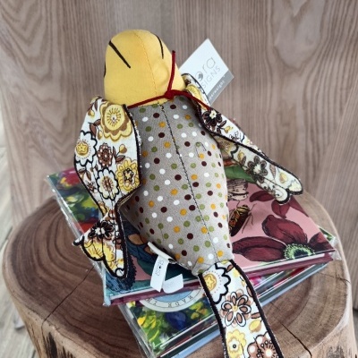 Pelucha de pássaro com padrões florais e bolinhas sobre CDs num tronco de madeira