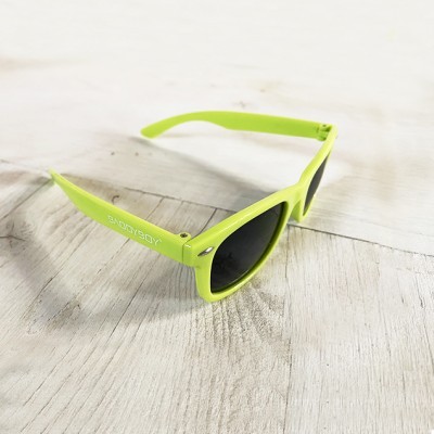 Óculos de sol verdes com lentes pretas e texto SWAGBOY, sobre madeira clara.