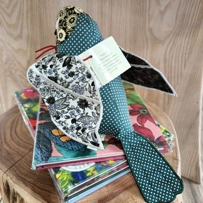 Boneco tecido em forma de pássaro colorido sobre cadernos coloridos num tronco de madeira