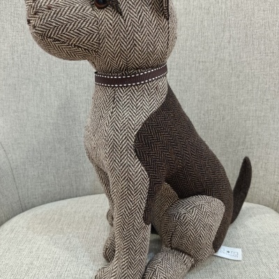 Boneco de cão de tecido castanho e bege sentado numa cadeira cinzenta clara