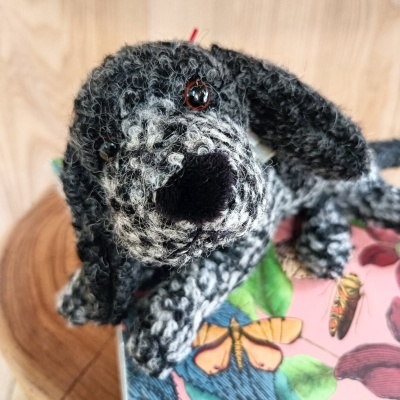 Pelúcia de cão cinza e preta sobre caixa colorida com padrão de borboletas