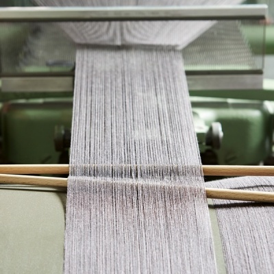 Máquina de tecer fios cinzentos com varas de madeira e mão ajustando