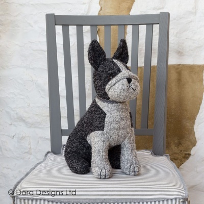 Pelúcia de cão preto e cinza sentada numa cadeira cinza com almofada riscada