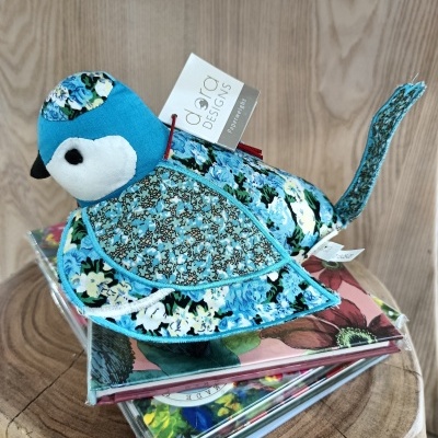 Pássaro de tecido azul decorativo com padrões florais sobre livros coloridos