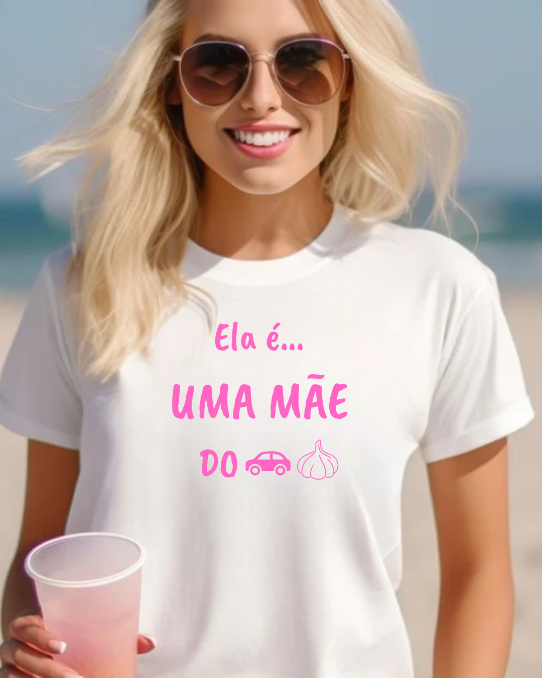 T-shirt branca com texto em rosa e ícones, usada por mulher loira com óculos de sol na praia