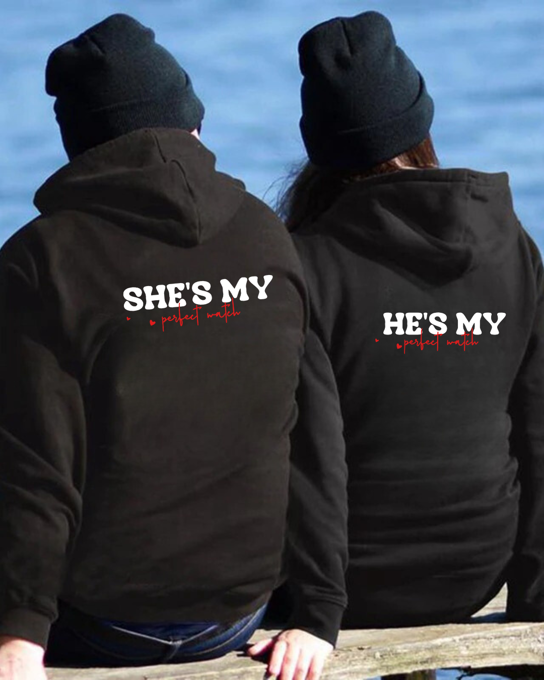 Casal com hoodies pretos e gorros pretos sentados de costas junto à água