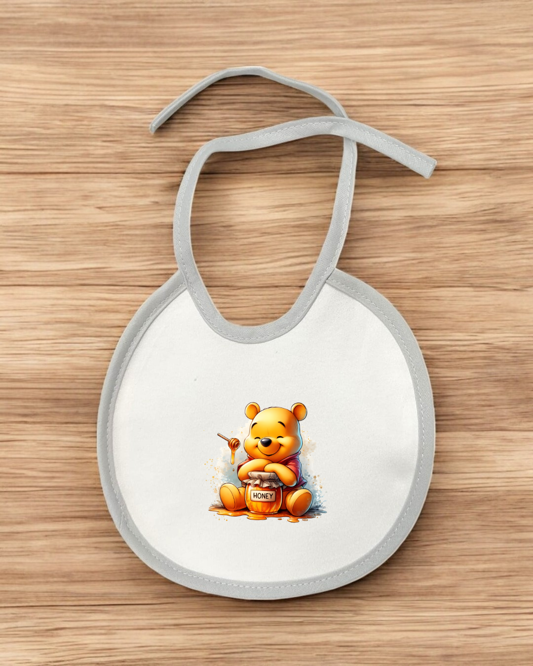 Babete branco com borda cinza e desenho do ursinho Pooh com pote de mel