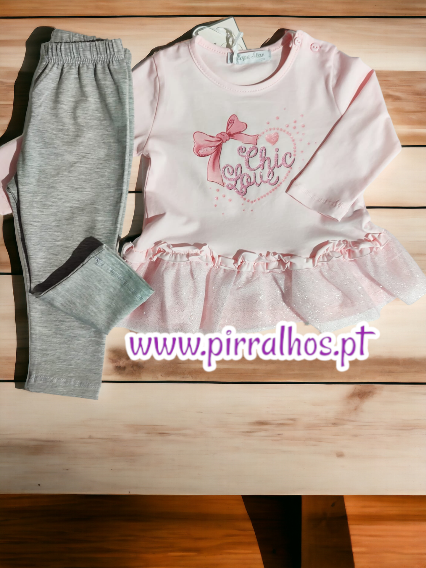 Conjunto de roupa para bebé rosa e cinzenta sobre mesa de madeira