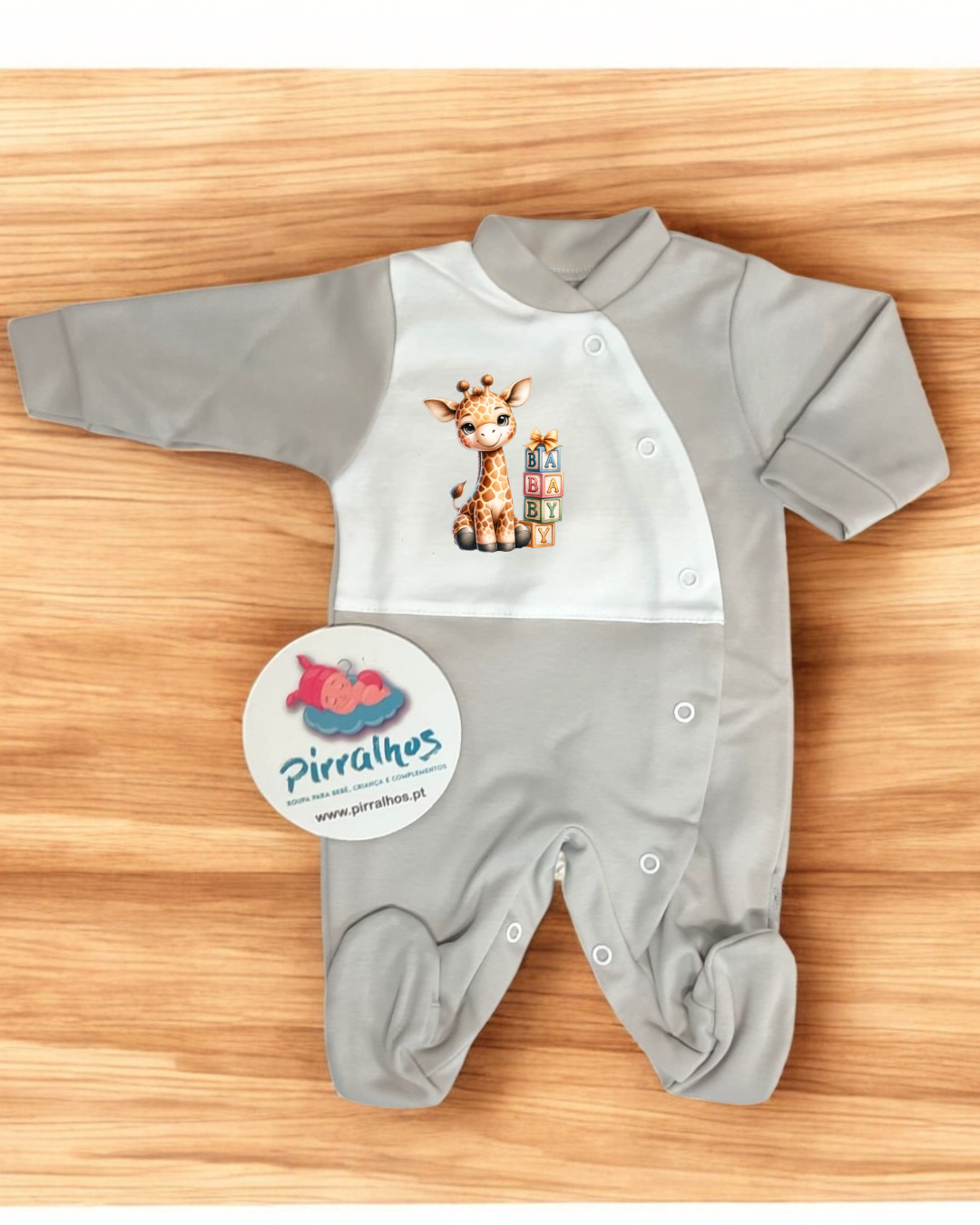 Babygrow cinzento claro com estampa de girafa e blocos coloridos, sobre madeira com etiqueta da marca