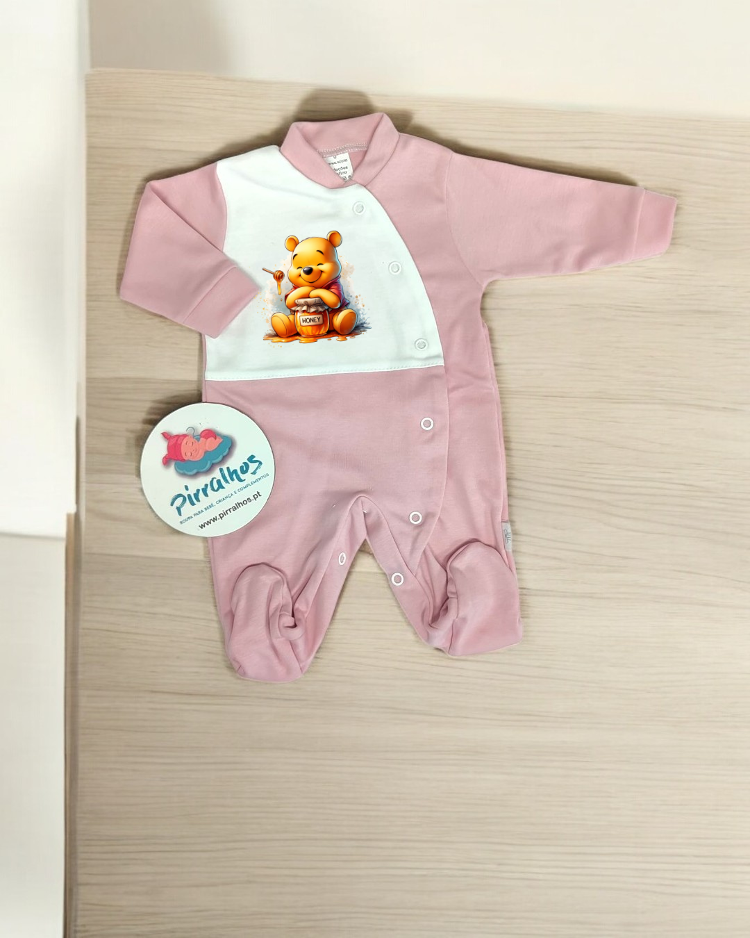 Macacão de bebé rosa e branco com urso amarelo estampado e botões frontais.