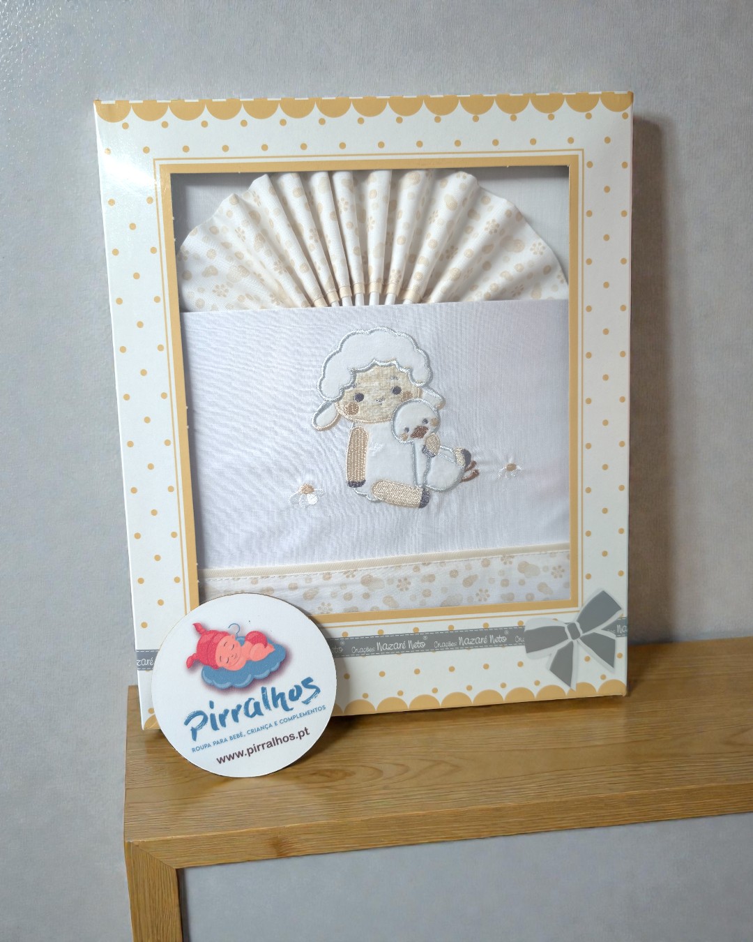 Conjunto de roupa de bebé branco e bege com bordado de ovelha e pato numa caixa com padrão de bolinhas.