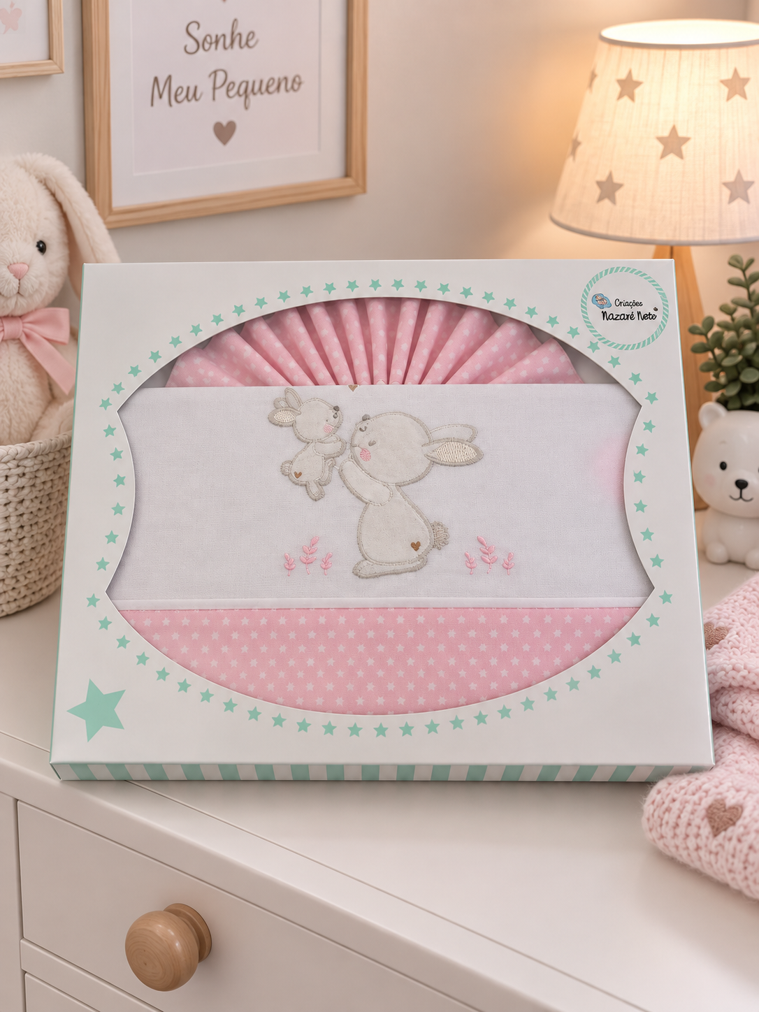 Conjunto de roupa de bebé rosa com coelhos bordados numa caixa branca decorada com estrelas verdes