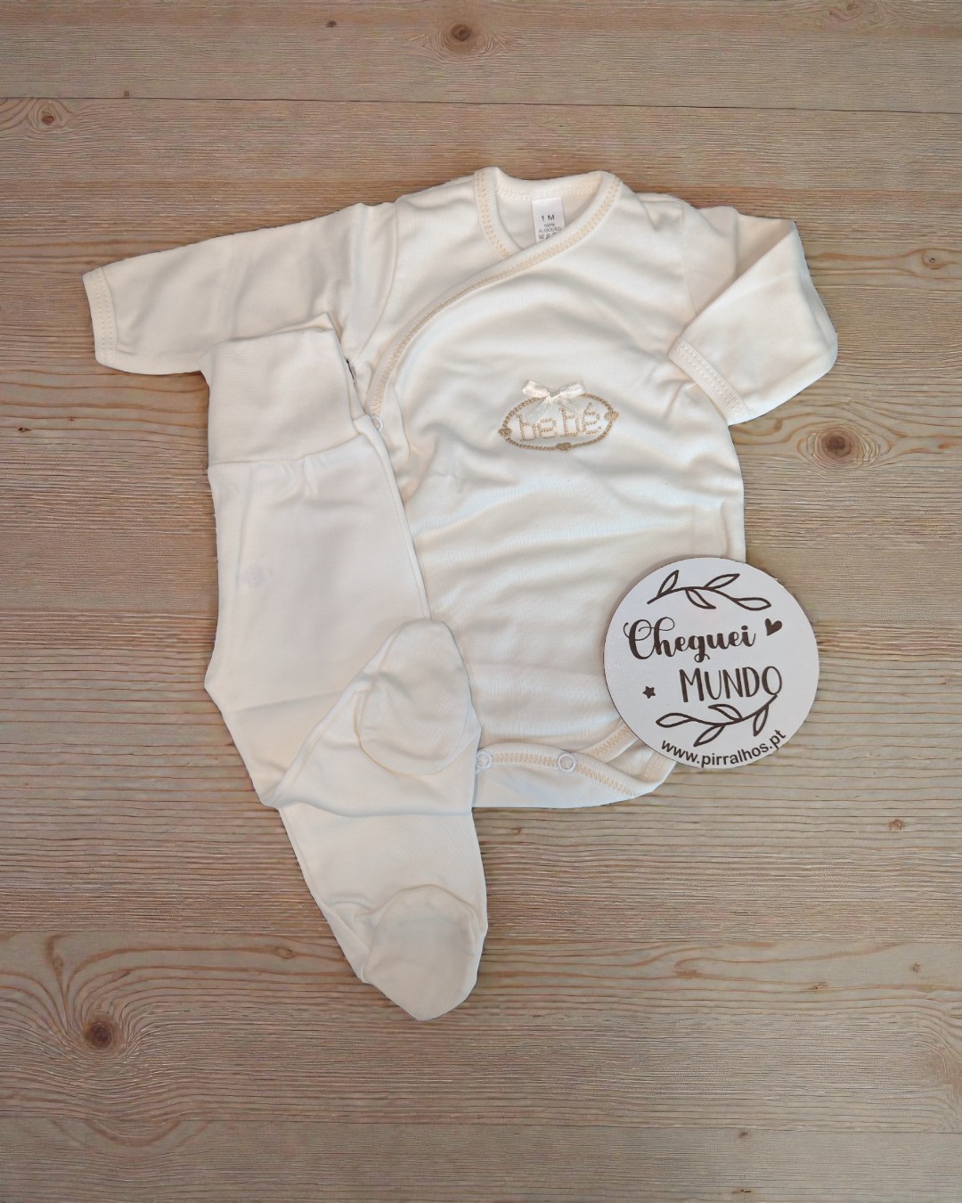 Conjunto branco de roupa para bebé com body de mangas compridas e calças com pés, em algodão, sobre fundo de madeira.