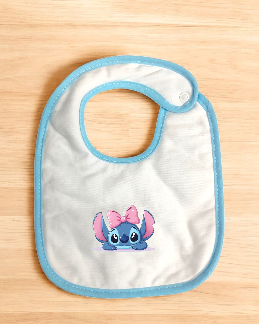 Babete branco com bordas azuis e personagem cartoon azul com laço rosa