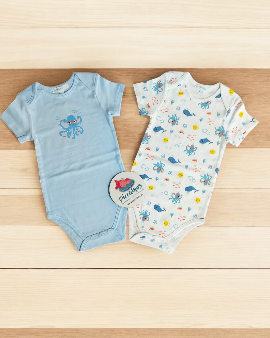 Dois bodies de bebé com estampas marinhas sobre superfície clara de madeira