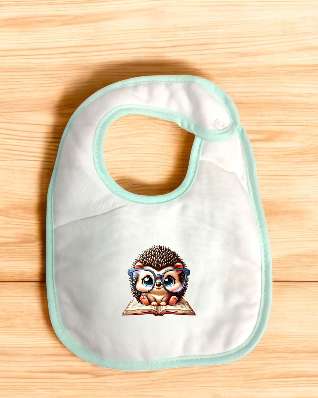 Babete branco com estampa de ouriço com óculos e livro sobre fundo de madeira clara