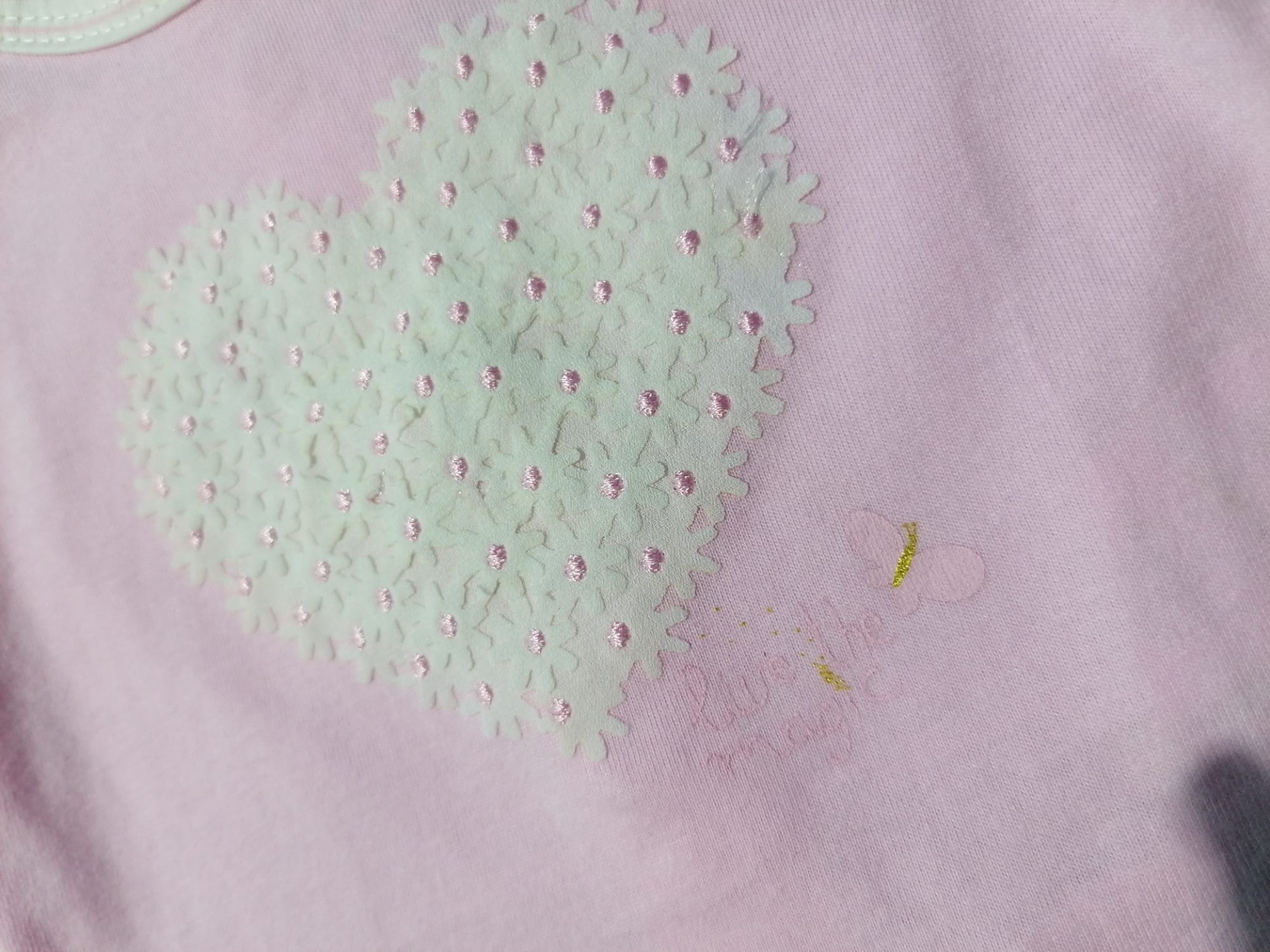 Tecido cor-de-rosa com bordado de coração branco e pequenos pontos cor-de-rosa.