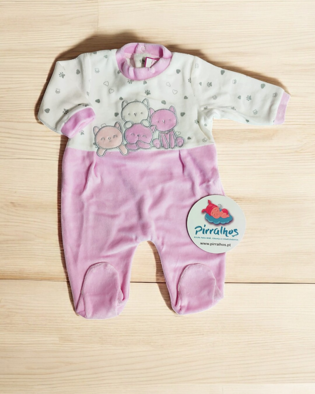 Macacão de bebé branco e rosa com desenho de animais e etiqueta Pirralhos sobre fundo de madeira clara