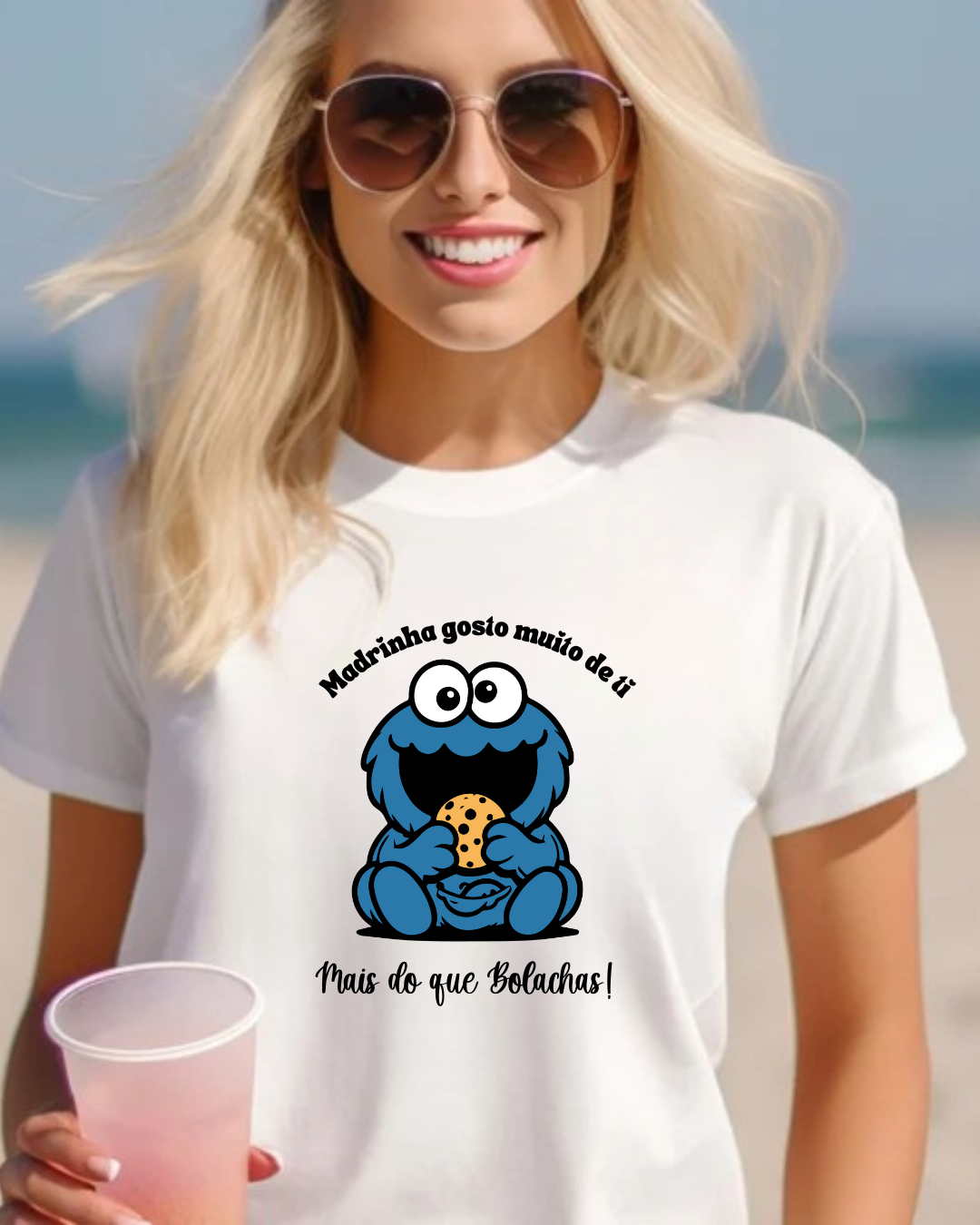 Camisola branca com estampa do Monstro das Bolachas e textos em português, usada por mulher loira com óculos de sol.