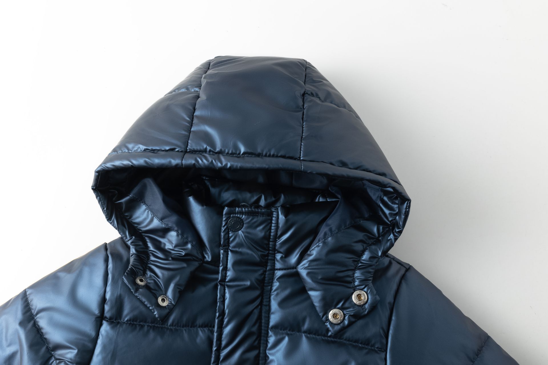 Casaco azul escuro acolchoado com capuz removível e botões de pressão