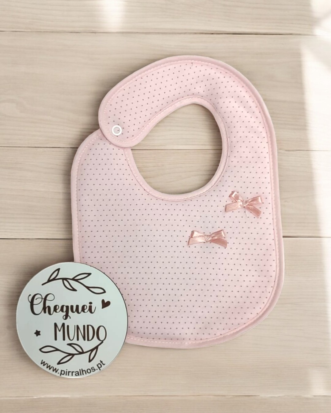 Babete cor-de-rosa claro com laços e placa redonda com texto Cheguei MUNDO
