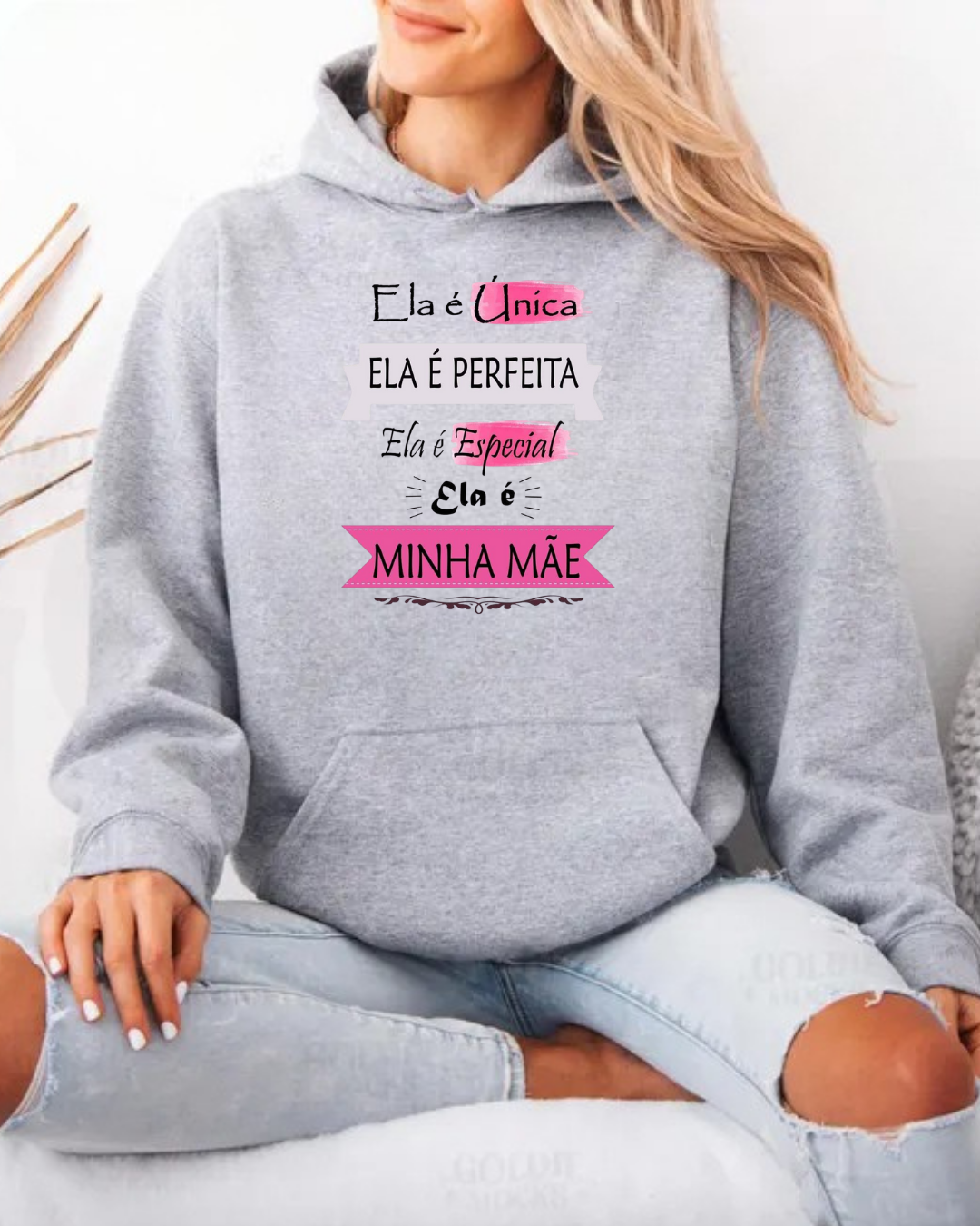 Mulher sentada a usar sweatshirt cinza clara com capuz e texto colorido sobre mães.