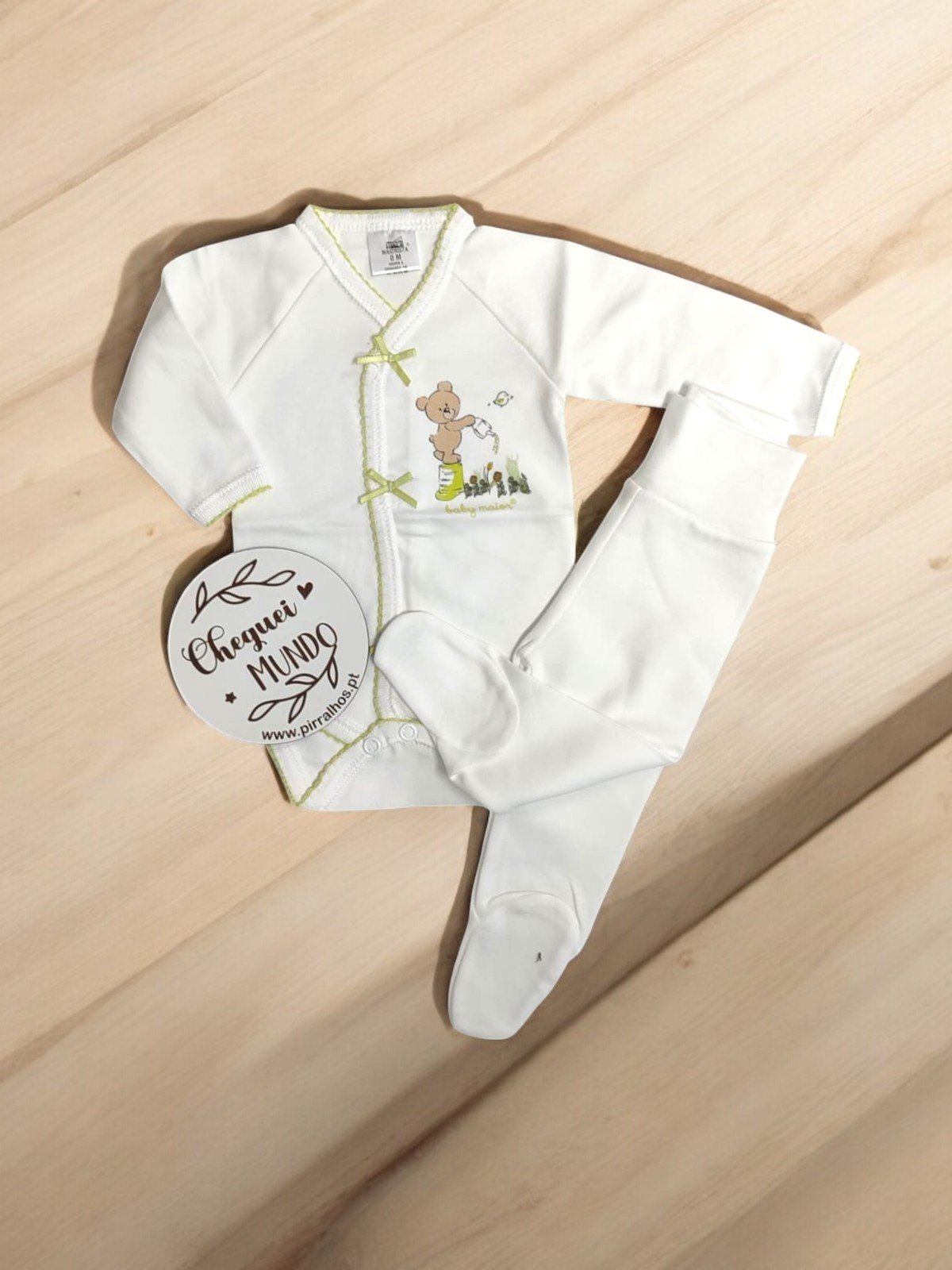 Conjunto de bebé branco com camisola de urso e calças com pés sobre madeira clara