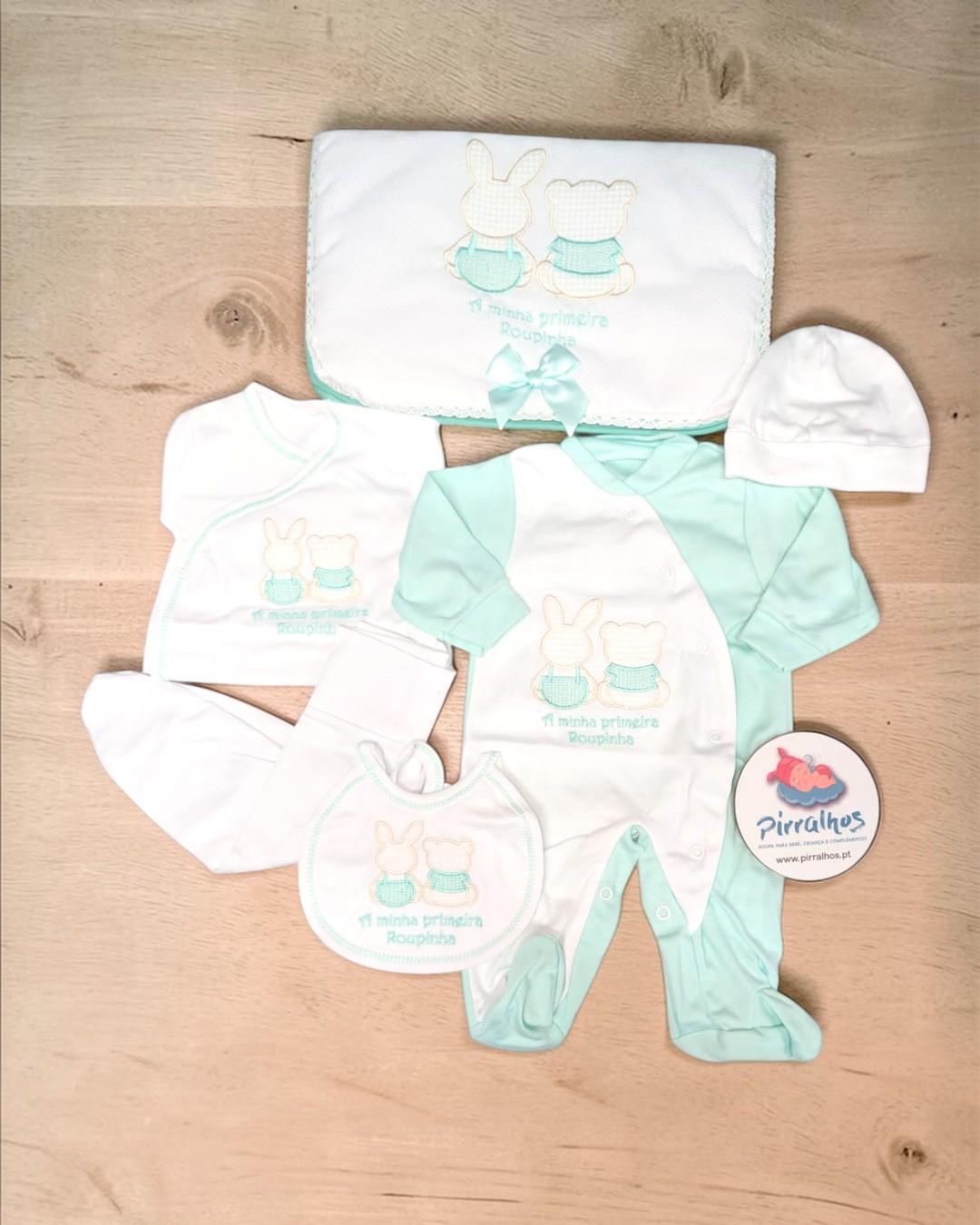 Conjunto de roupa de bebé em branco e verde água com bordados e manta com laço.