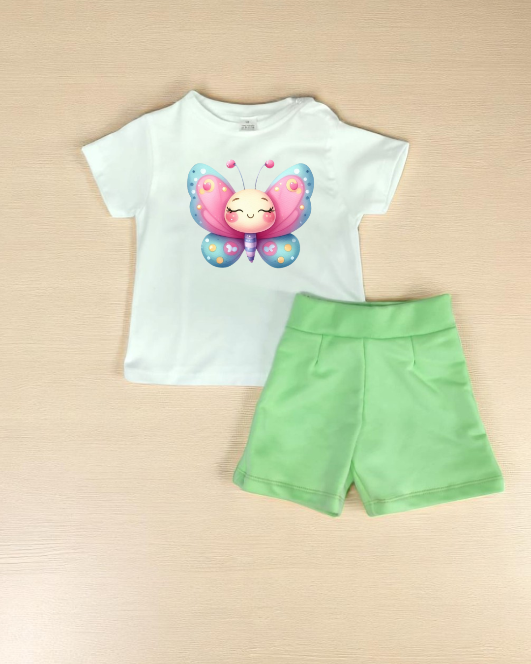 Conjunto infantil com t-shirt branca e calção verde claro sobre mesa de madeira