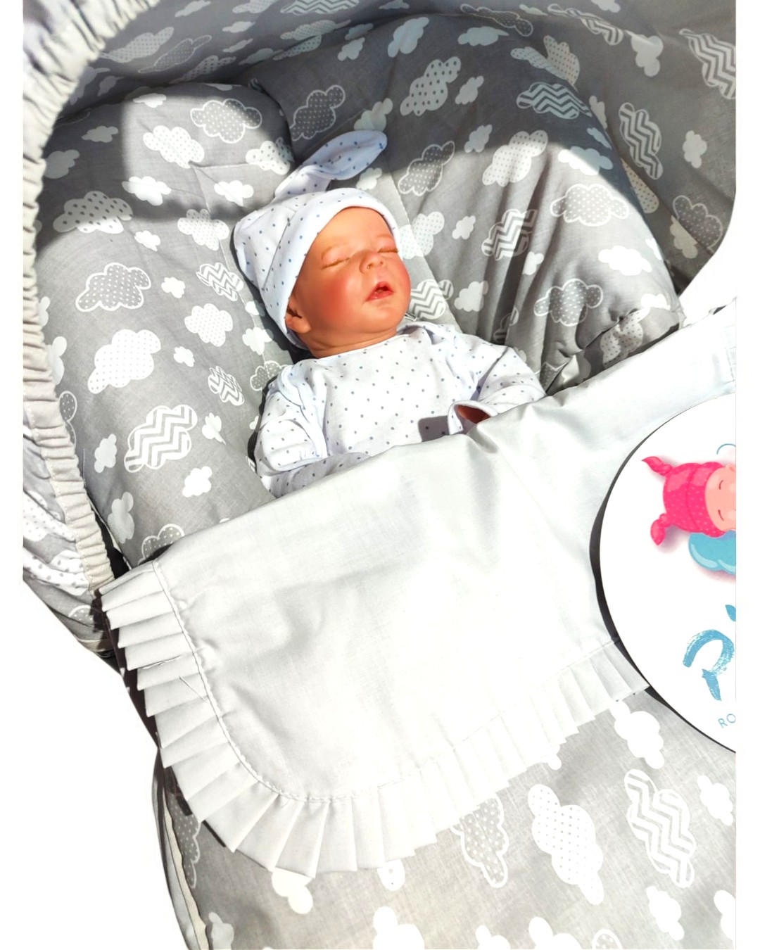 Ninho de bebé cinzento com padrão de nuvens e bebé vestido com pijama branco e gorro