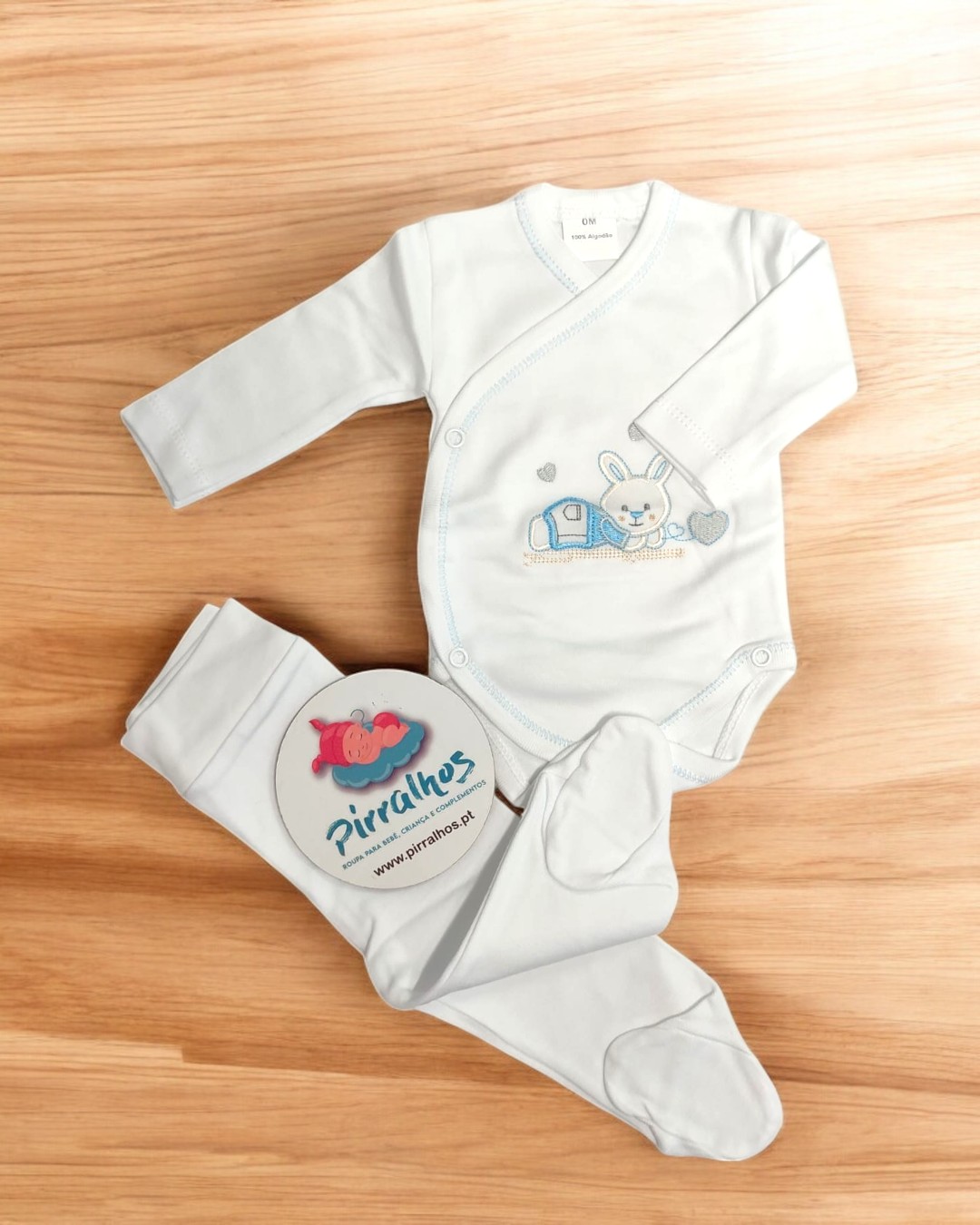 Conjunto de roupa de bebé branco com body e calças com pezinhos sobre madeira clara