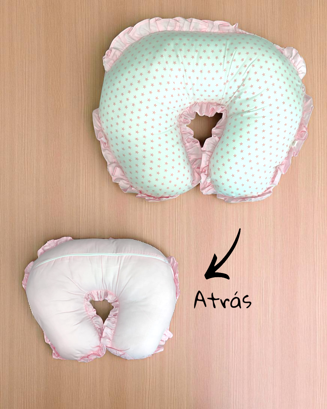 Almofada de amamentação em forma de U com padrão de estrelas rosa, texto 'Atrás', fundo madeira clara
