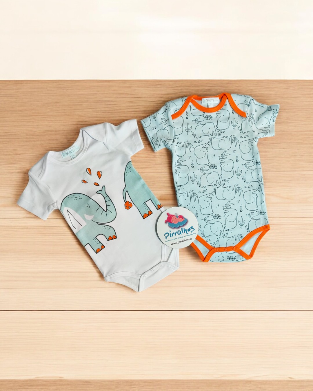 Dois bodies de bebé com desenhos de elefantes, um branco com elefante grande azul e um azul claro com elefantes pequenos.