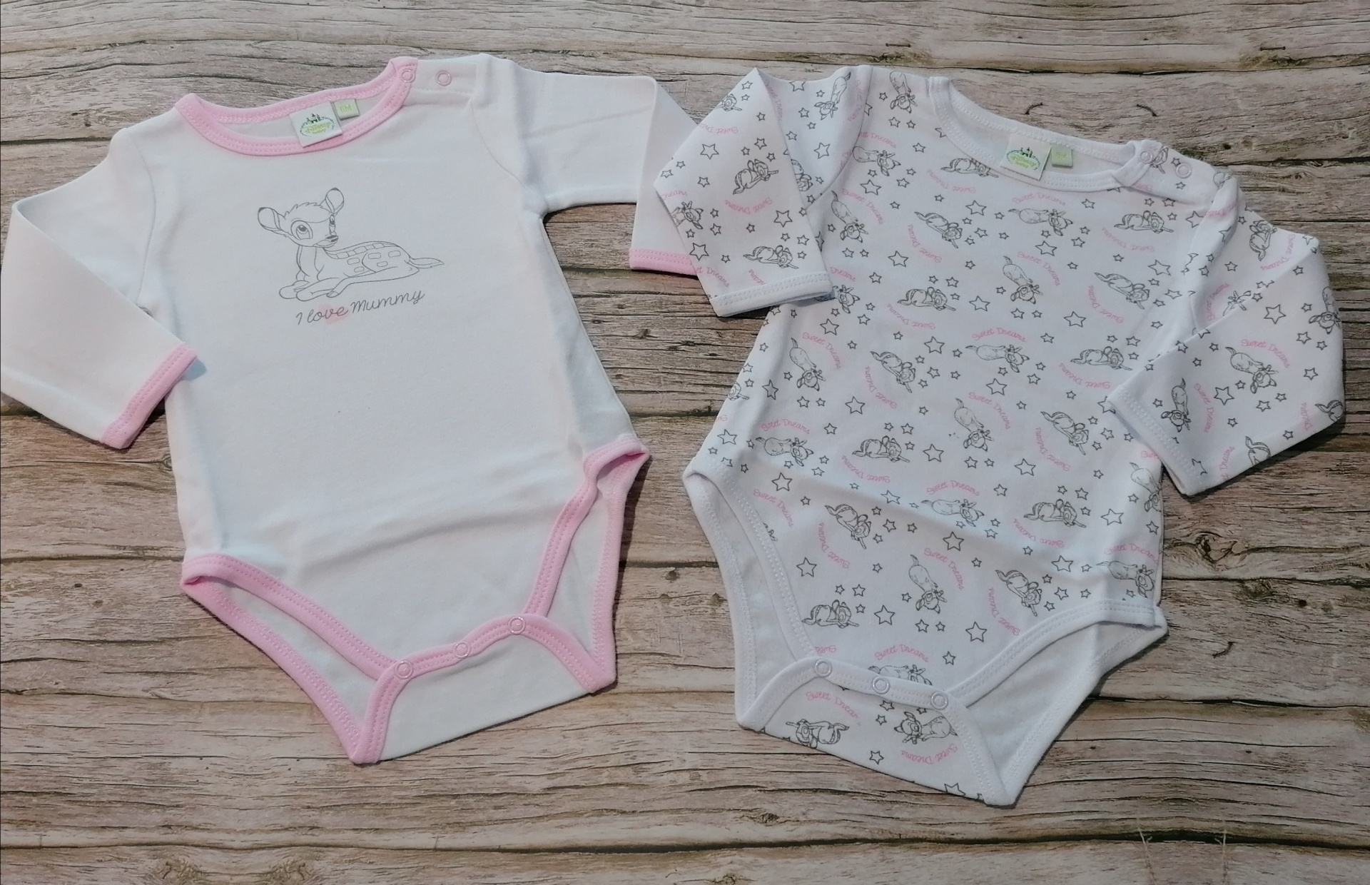 Dois bodies para bebé com manga comprida, um branco com bordas rosa e desenho de cervo, outro branco com padrão floral e cervos