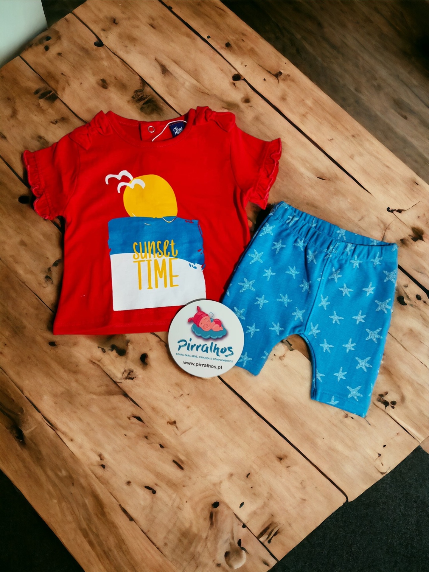 Conjunto infantil com t-shirt vermelha e bermuda azul sobre mesa de madeira