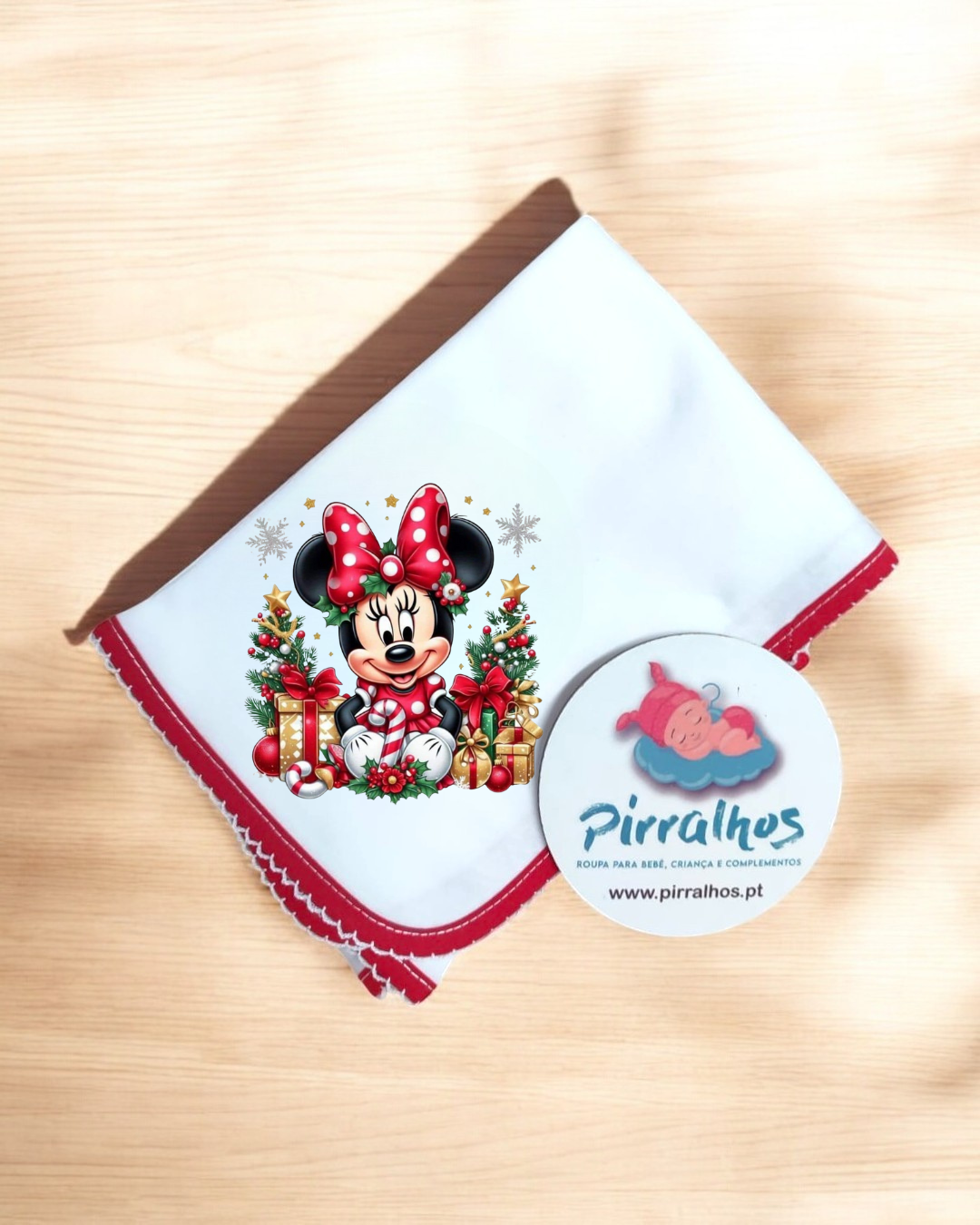 Babete branco com borda vermelha e ilustração natalícia da Minnie e etiqueta redonda da marca Pirralhos.